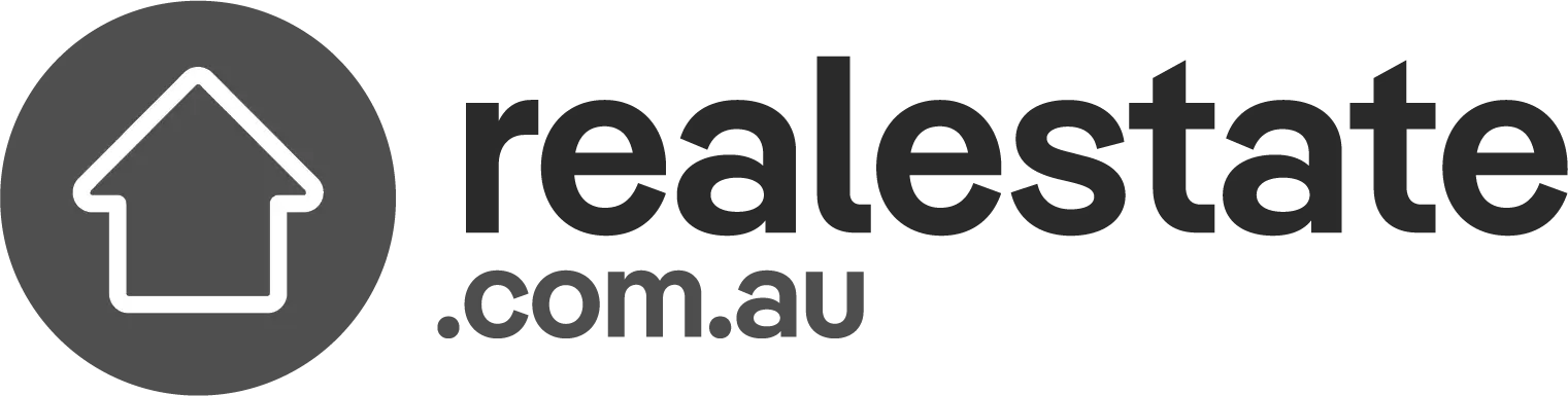 Logo of realestate.com.au, featuring a white outline of a house within a dark circular background on the left. To the right of the circle, the text "realestate.com.au" is depicted in bold, sans-serif font, embodying simplicity and modernity for those seeking the best duplex designs by renowned Sydney architects.